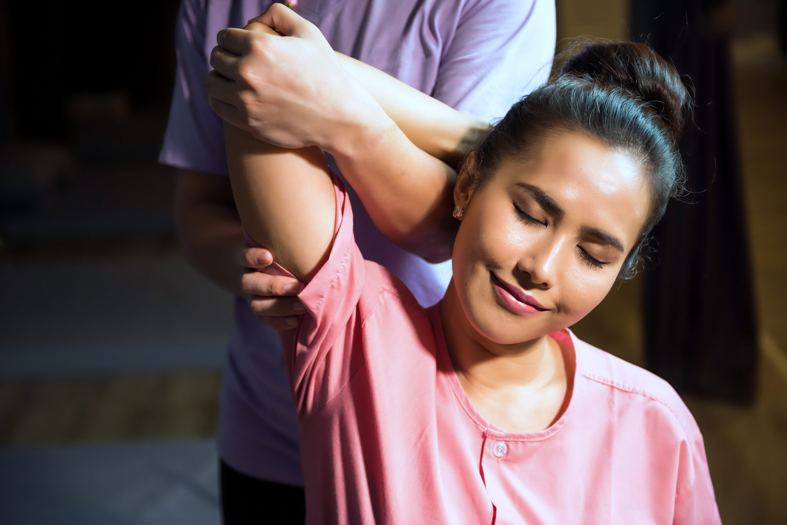 Woman receiving assisted shoulder stretch from therapist in wellness studio